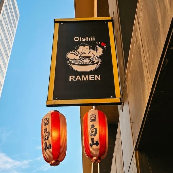 Oishii Ramen sign with a sumo wrestler logo and two red lanterns hanging below it.